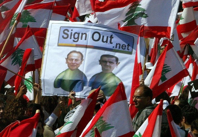 Lebanese demonstrators hold up a caricature with Lebanese President Emile Lahoud (R) and his Syrian counterpart Bashar al-Assad portrayed as two MSN contacts with a "sign out" button amid a sea of Lebanese flags in Beirut's downtown 14 March 2005. An emboldened Lebanese opposition mobilized more than 800,000 people to demand an end to Syrian military domination of Lebanon, hurling a potent challenge to the Syrian-backed government. AFP PHOTO/ANWAR AMRO / AFP PHOTO / ANWAR AMRO