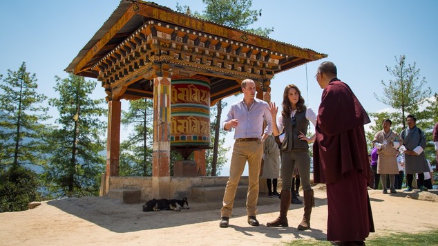 They speak with a monk near a prayer wheel