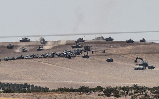 This picture taken from the Turkish Syrian border city of Karkamis in the southern region of Gaziantep, on August 24, 2016 shows Turkish army tanks and pro-Ankara Syrian opposition fighters moving two kilometres west from the Syrian Turkish border town of Jarabulus. Turkey's army backed by international coalition air strikes launched an operation involving fighter jets and elite ground troops to drive Islamic State jihadists out of a key Syrian border town. Turkey's state-run Anadolu news agency reported that pro-Ankara Free Syrian Army (FSA) rebels had already penetrated three kilometres (two miles) inside Syria towards the IS-held town of Jarabulus. The air and ground operation, the most ambitious launched by Turkey in the Syria conflict, is aimed at clearing jihadists from the town of Jarabulus, which lies directly opposite the Turkish town of Karkamis. / AFP PHOTO / BULENT KILIC