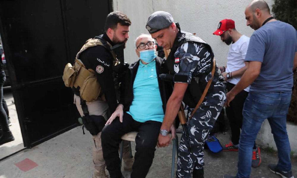 عنصران من الأمن يحملان مسناً إلى مركز الاقتراع
